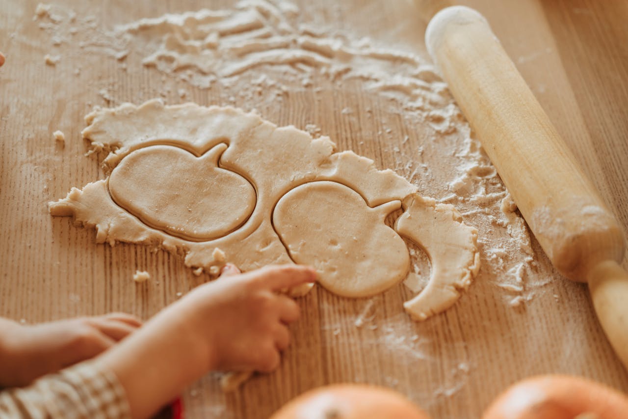 A child making pumpkin-shaped cookies with dough, perfect for Halloween or Thanksgiving.