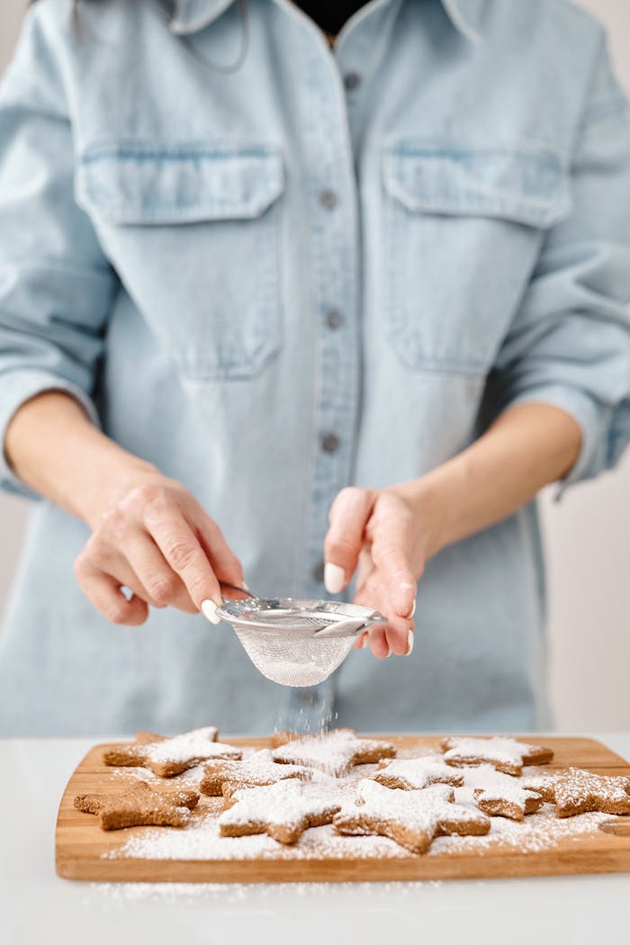 Close-up of a person decorating star-shaped cookies with powdered sugar, evoking a festive Christmas feel.